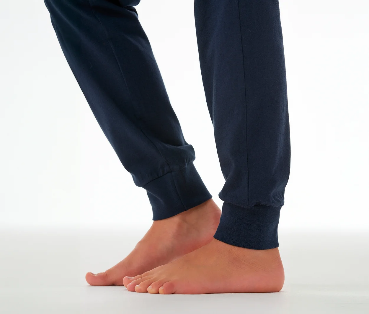 Kinderbeine in dunkelblauer SCHIESSER Kinder-Pyjamahose mit Bündchen, die Füße sind barfuß.