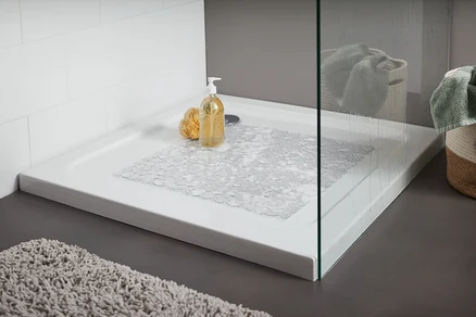 Duschwanne mit transparenter Duschwanneneinlage. Auf der Wanne liegen ein gelber Badeschwamm und eine Flasche mit Pumpspender.