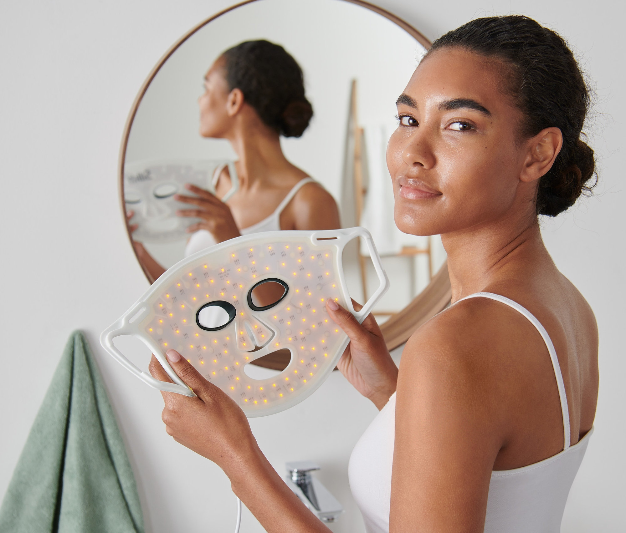 Frau hält Silk'n LED-Gesichtsmaske 100 vor dem Spiegel.