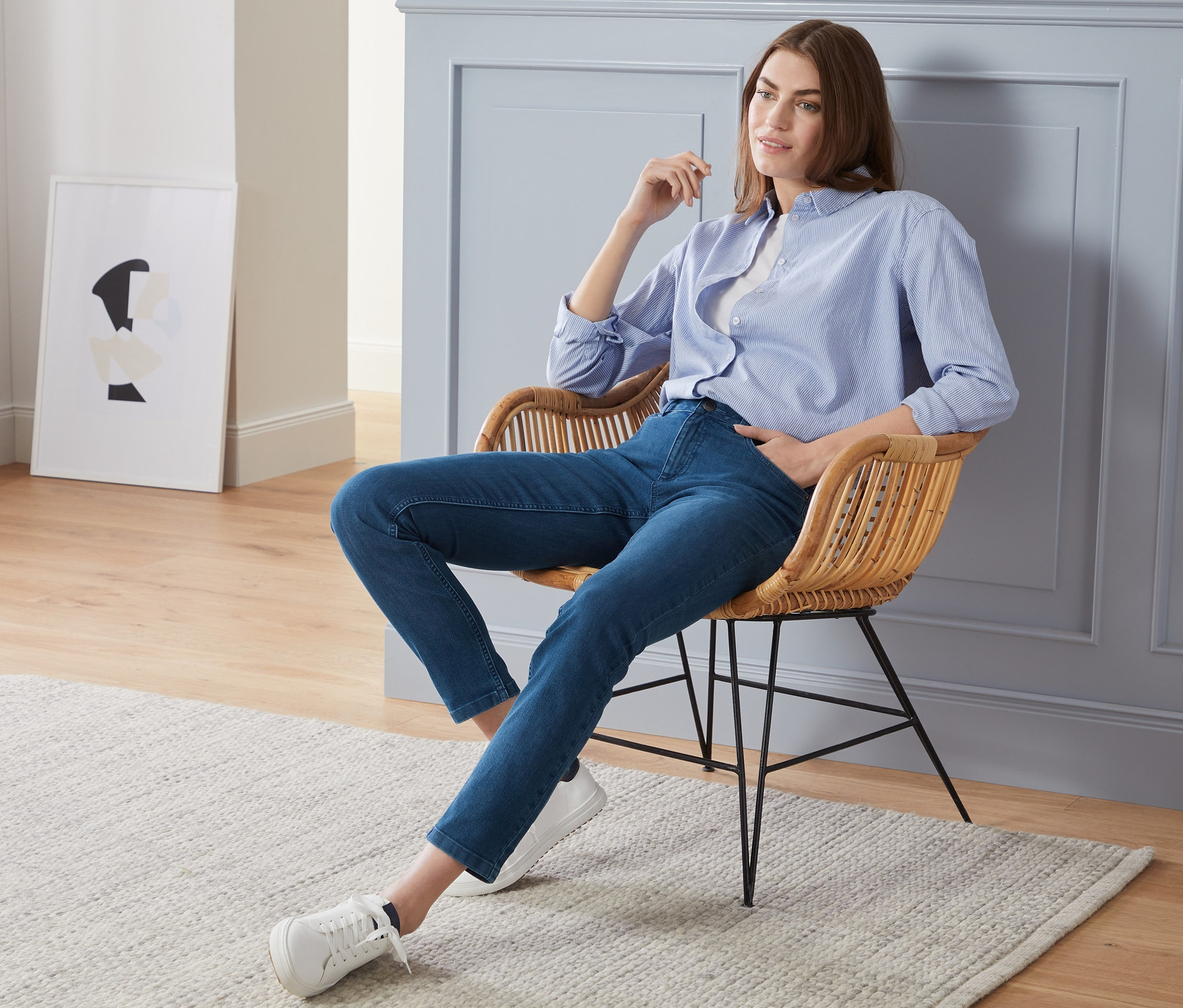 Frau sitzt in blauem Hemd und Slimfit-Jeans auf einem Stuhl.