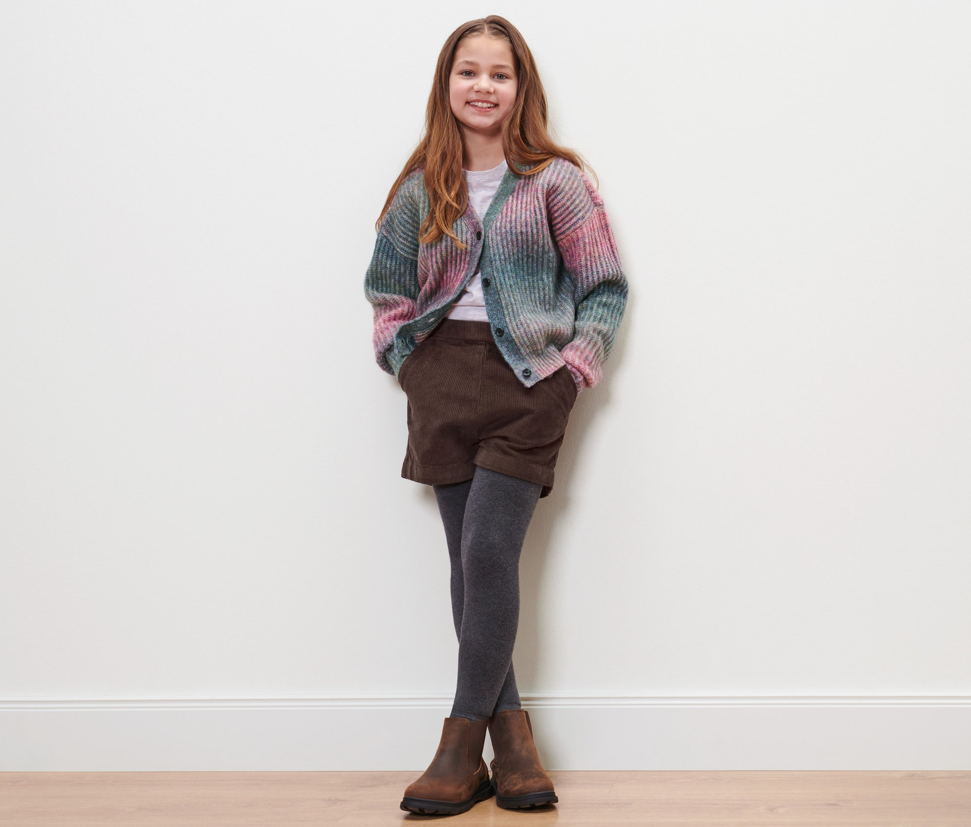 Ein Mädchen posiert und trägt Kinder-Cord-Shorts, einen Pullover und Schuhe.