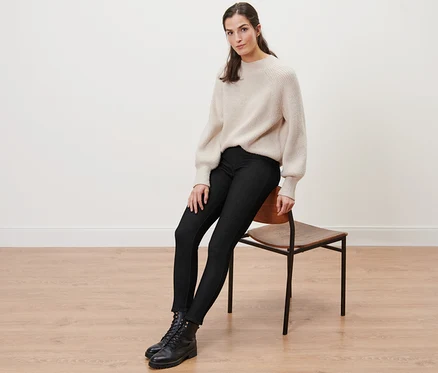 Frau sitzt auf einem Stuhl und trägt gefütterte Leggings in Jeansoptik, einen Pullover und Stiefel.