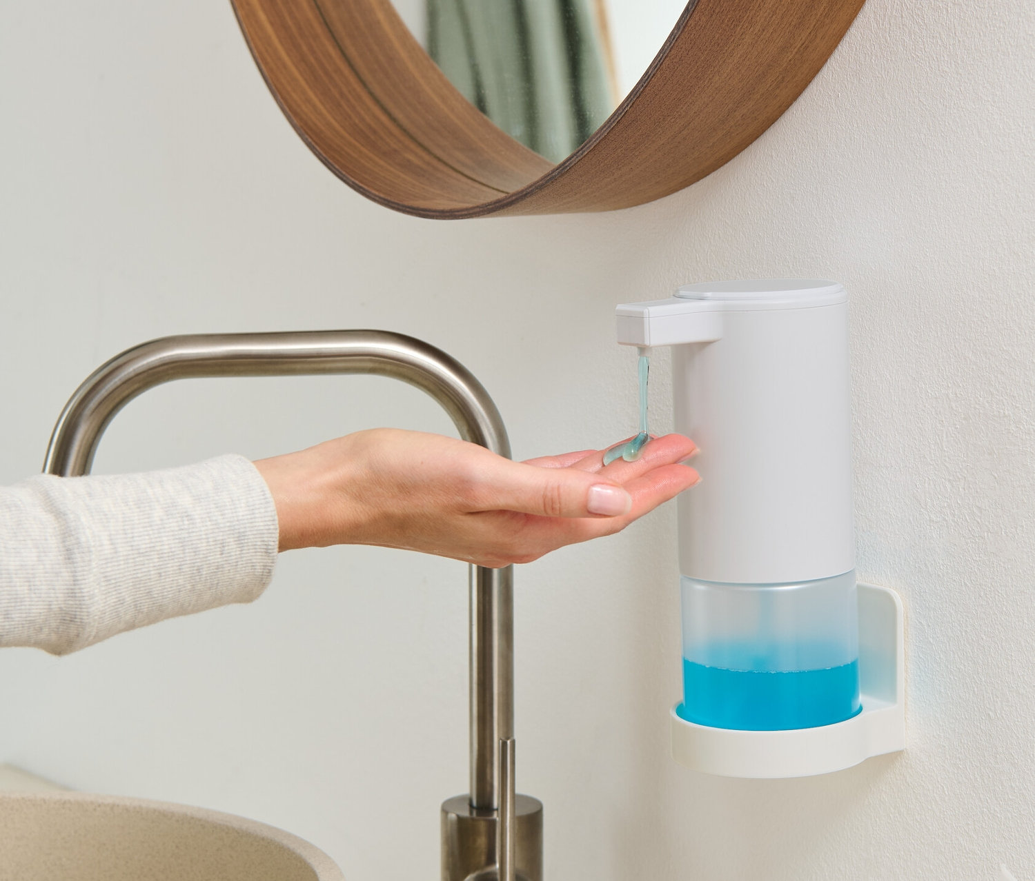 Eine Frau gibt sich Seife aus einem weißen Seifenspender mit Sensor in die Hand, der an der Wand montiert ist.