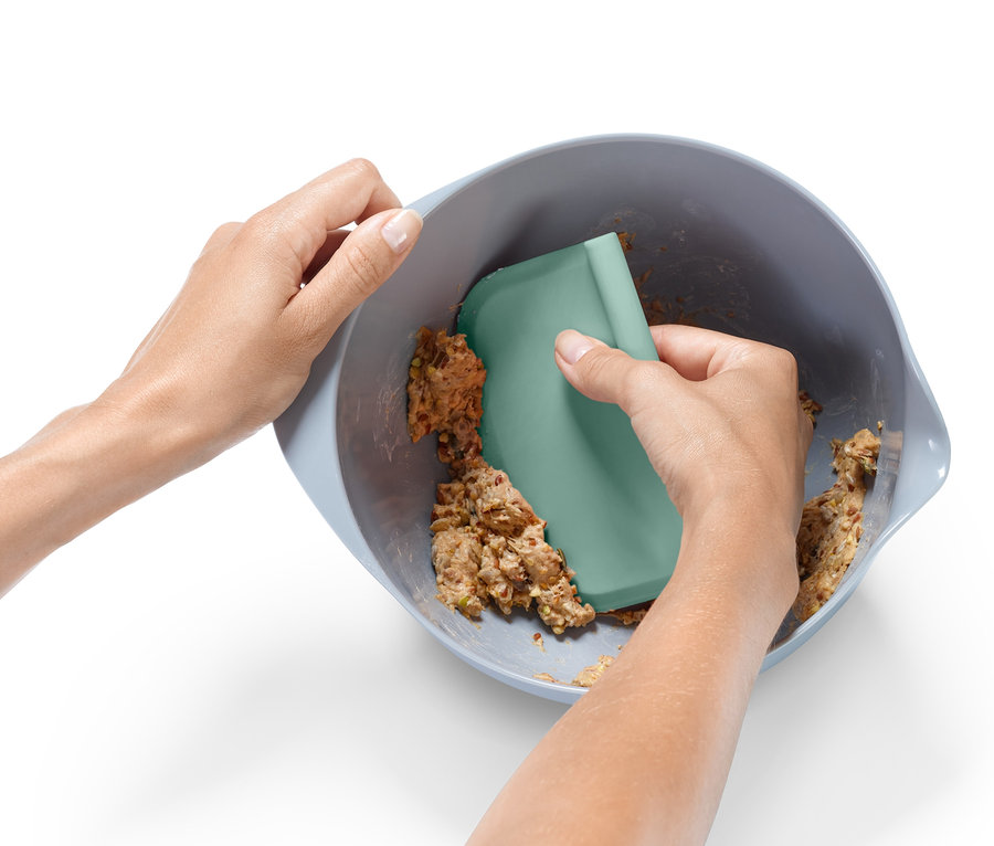 Zwei Hände vermengen Teig in einer Schüssel mit einem grünen Schaber aus dem Profi-Backhelfer-Set.