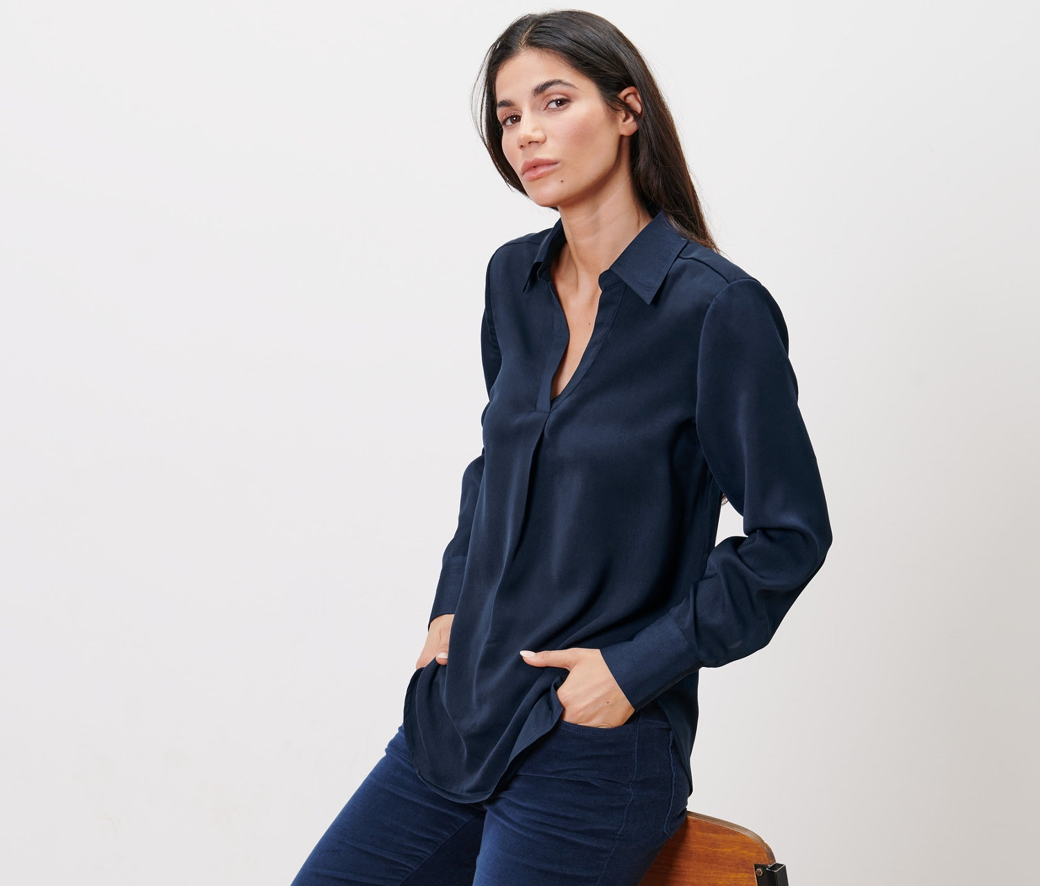 Frau sitzt auf einem Stuhl und trägt eine Satin-Bluse.