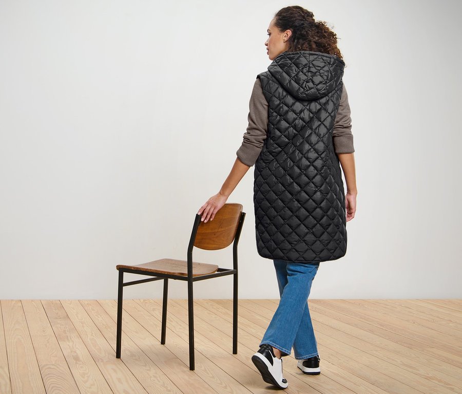 Frau posiert in langer Steppweste mit Kapuze.