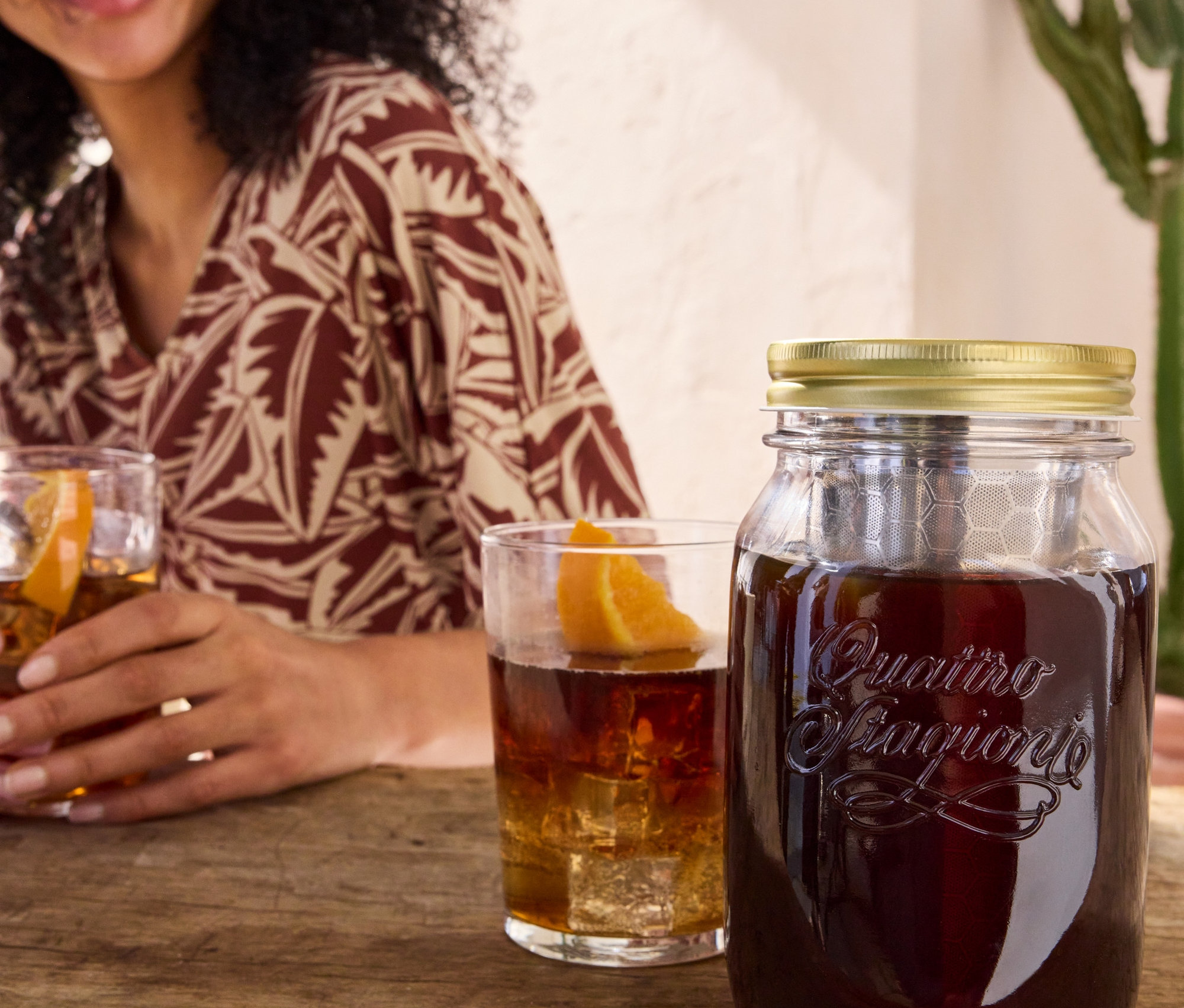 Frau hält Glas mit Getränk neben Cold Brew Maker »BrewJar« und bedrucktem Jerseykleid.
