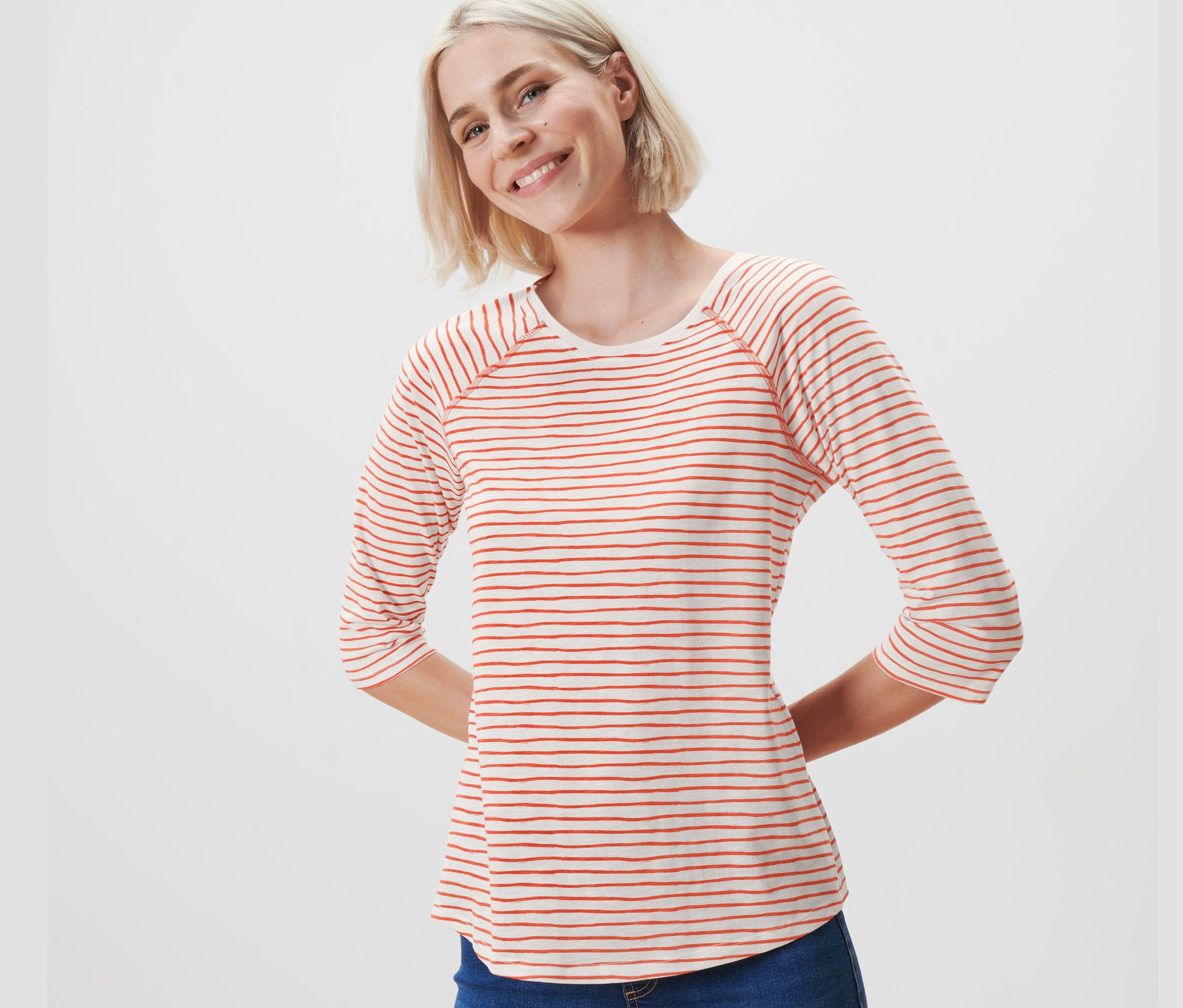 Frau mit blonden Haaren trägt ein gestreiftes Shirt mit 3/4-Arm und Jeans.