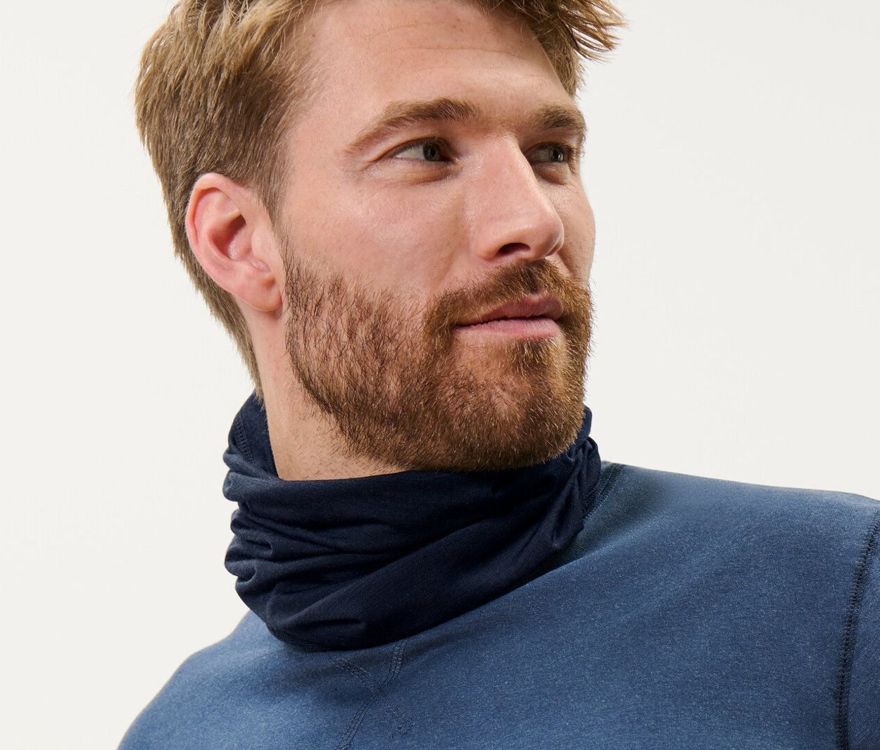 Mann mit braunen Haaren trägt ein blaues Multifunktionstuch mit RWS-zertifizierter Wolle und ein blaues Oberteil.