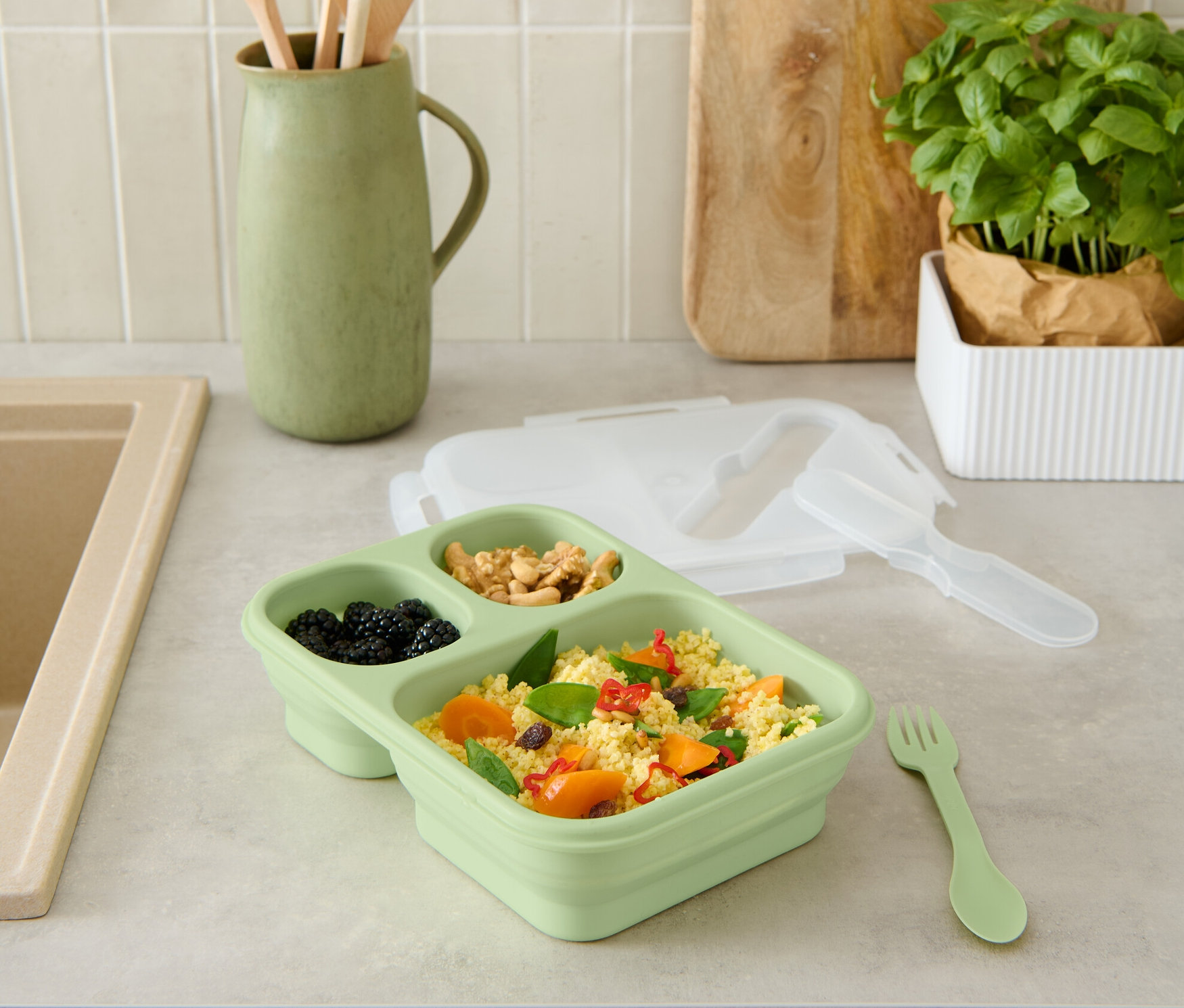 Eine grüne, faltbare Lunchbox mit Essen auf einer Küchentheke.