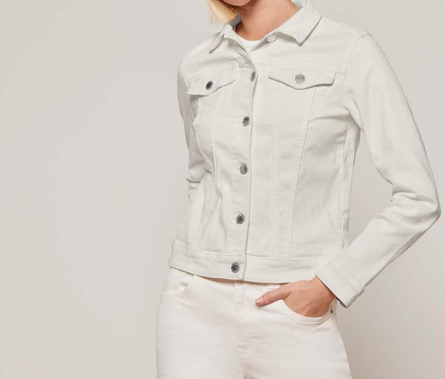 Frau posiert in cremefarbener Jeansjacke und grauer Mütze.