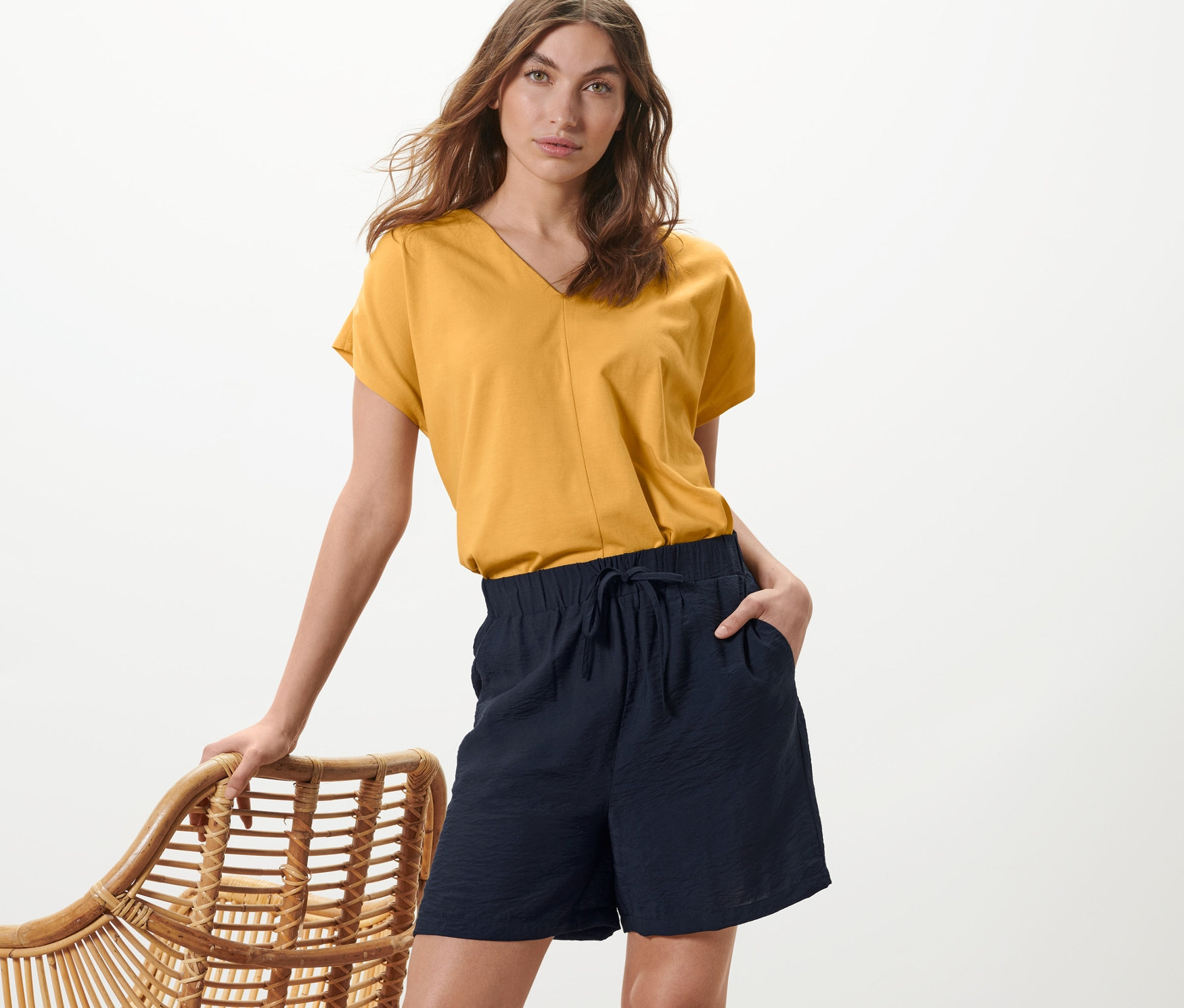 Frau posiert in gelbem Oberteil und dunkelblauen Shorts.