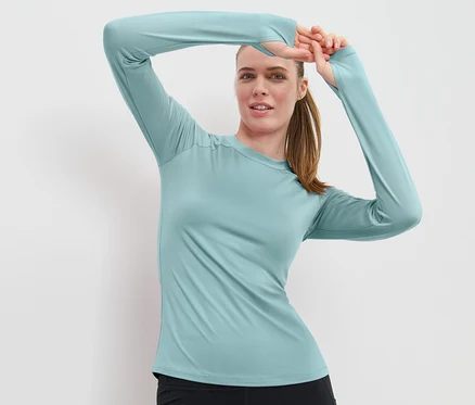 Frau posiert mit den Händen über dem Kopf in einem hellblauen Langarm-Funktionsshirt.