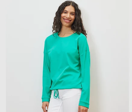 Frau trägt ein Sweatshirt in Aqua und eine weiße Hose.