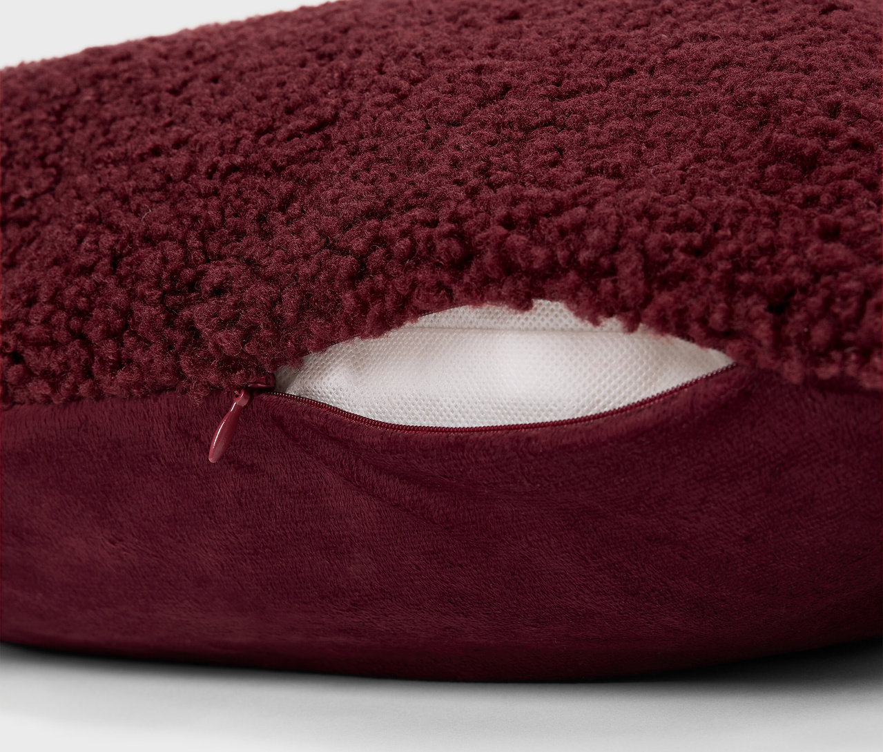 Detail eines burgunderroten, zotteligen Kissens mit Reißverschluss.