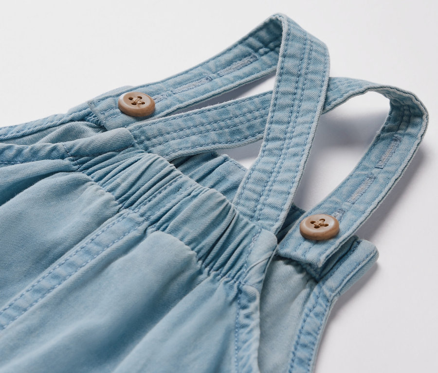 Detailaufnahme einer Kinder Chambray-Latzhose mit Holzknöpfen.