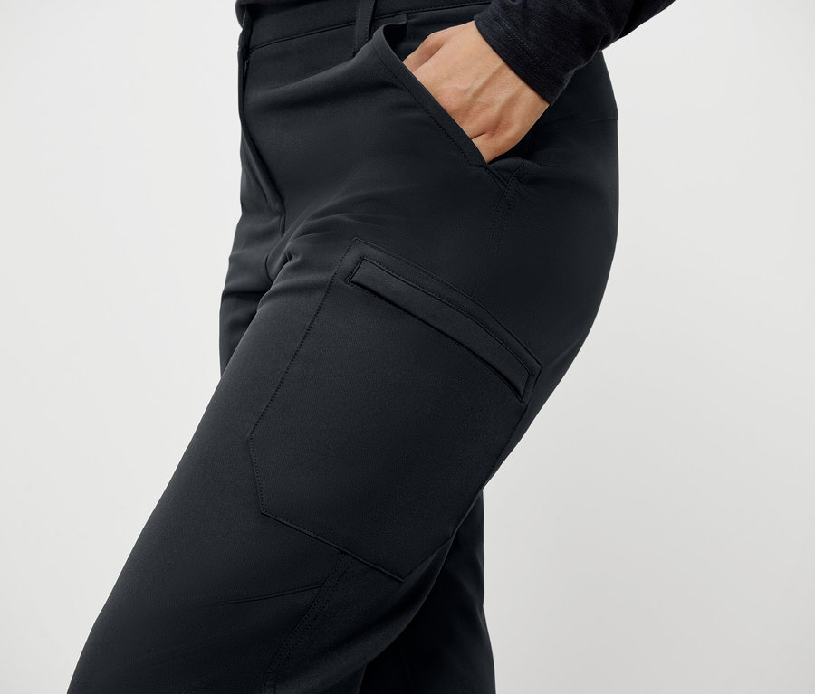 Detailaufnahme einer Frau, die eine schwarze Hose mit Taschen trägt und eine Hand in der Hosentasche hat.