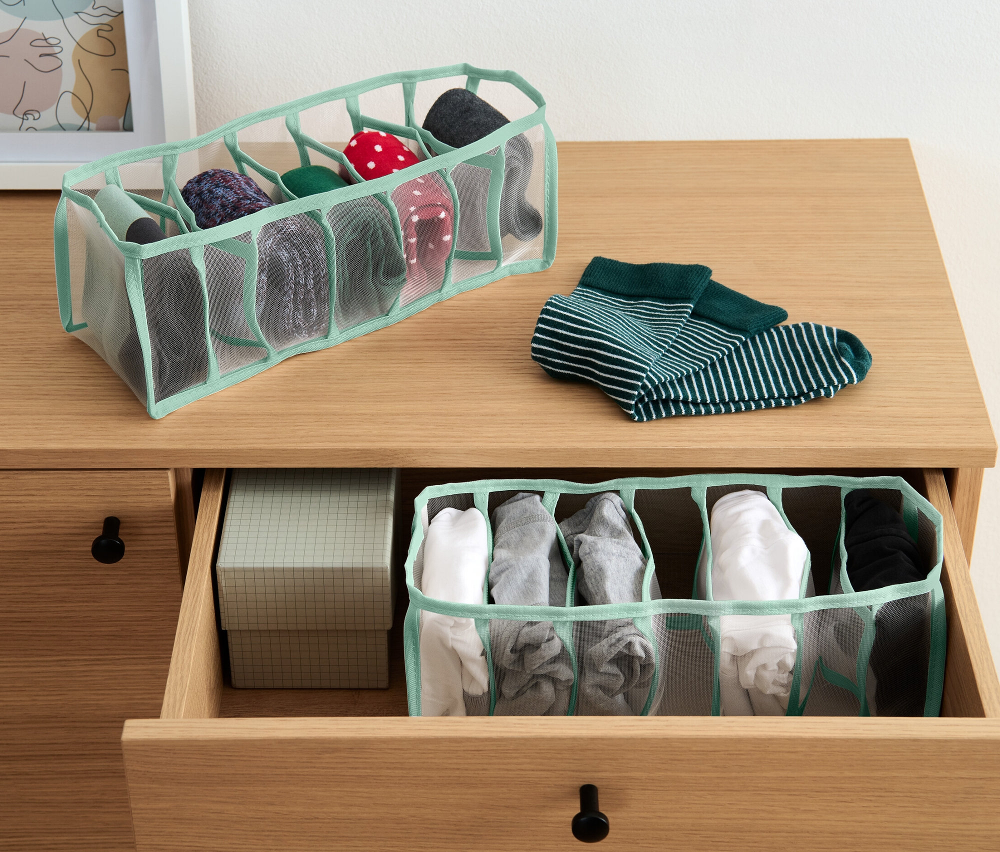 Zwei Kleiderschrank-Organizer, einer auf der Kommode und einer in einer offenen Schublade, beide mit diversen Socken.