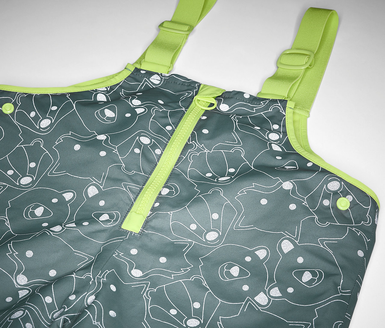 Detail einer Kinder-Thermo-Regenhose mit reflektierenden Elementen, grau mit Bären- und Fuchsprint und gelben Trägern.