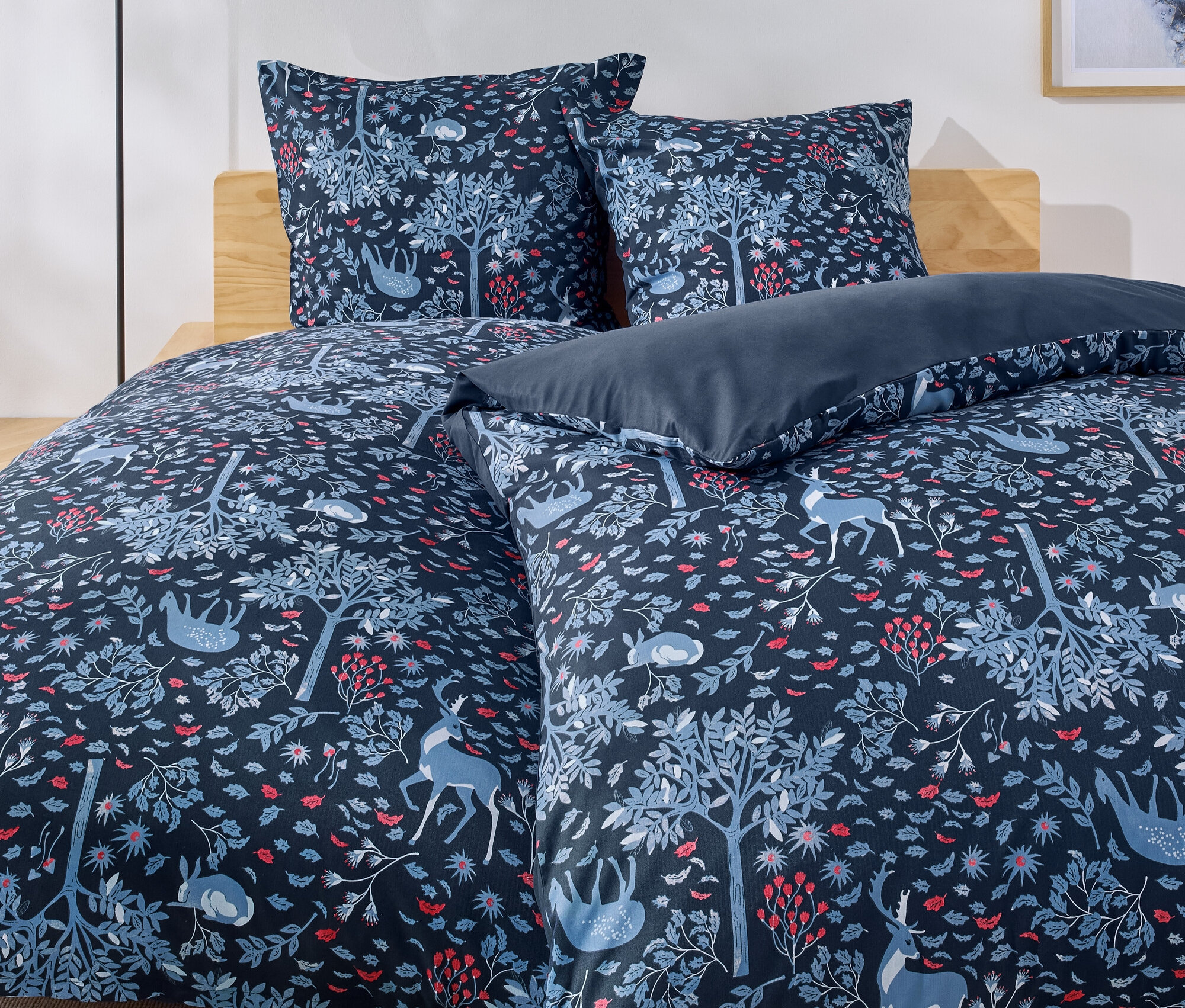 Bett mit blauer Bettwäsche mit Wald-, Baum-, Hirsch- und Kaninchenmuster.