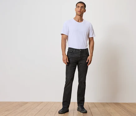 Mann steht auf Holzboden, trägt schwarze Jeans und weißes T-Shirt.