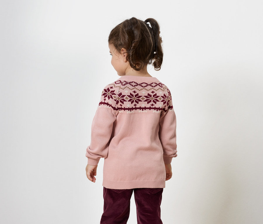 Mädchen von hinten, trägt einen rosa Pullover mit bordeauxfarbenem Muster und bordeauxfarbene Hosen.