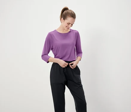 Frau bindet die Schnürsenkel an einer schwarzen Hose. Sie trägt ein lila Dreiviertelarmshirt.