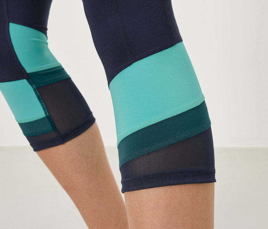Nahaufnahme von marineblauen Leggings mit türkisfarbenen und dunkelgrünen Einsätzen und Mesh-Details.