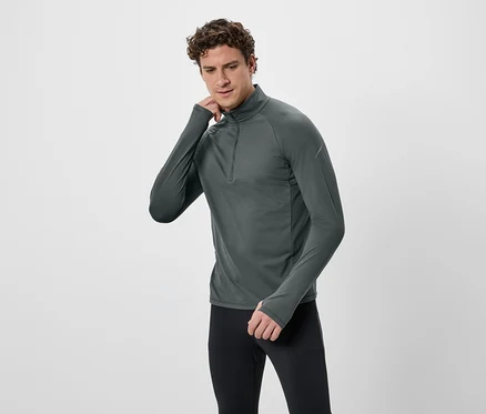 Mann mit lockigem Haar trägt ein graues Langarmshirt mit Reißverschluss und schwarze Leggings vor einem weißen Hintergrund.