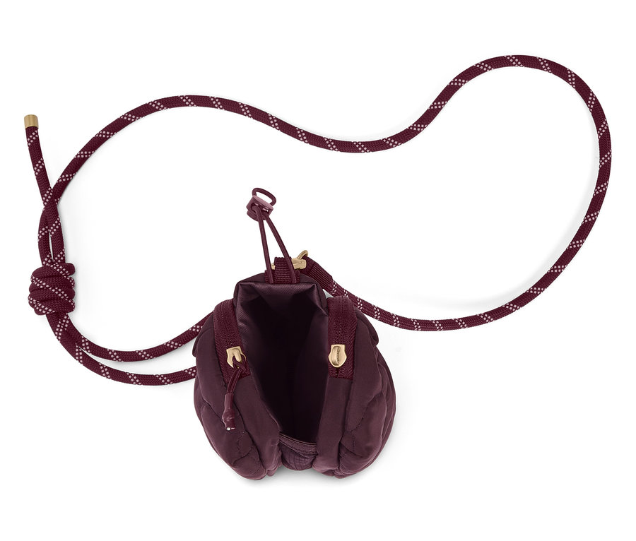 Draufsicht auf eine offene, bordeauxrote, gesteppte Handtasche mit Kordelriemen auf weißem Grund.