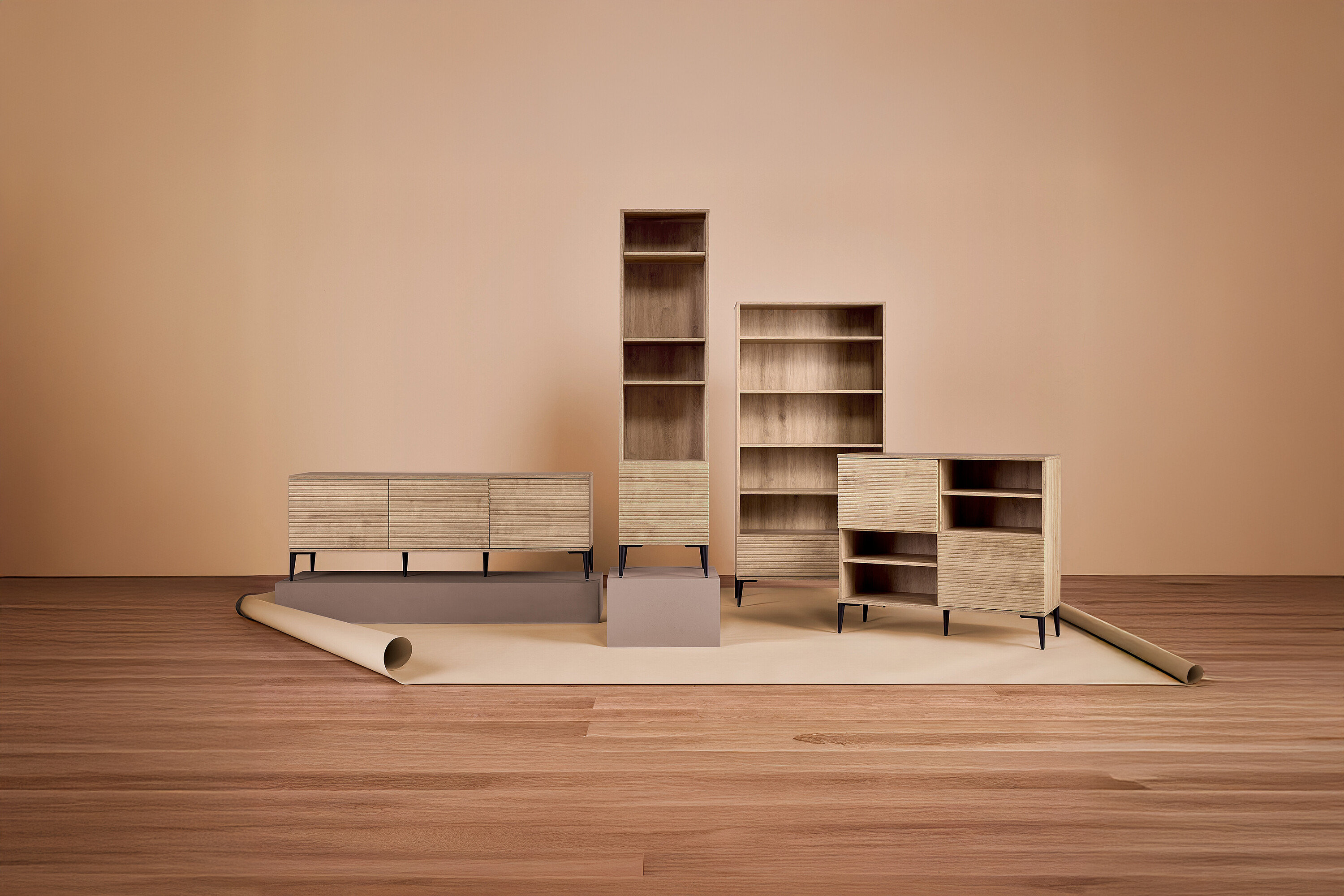 Verschiedene Holzmöbelstücke stehen auf einem hellen Teppich vor einer einfarbigen Wand.