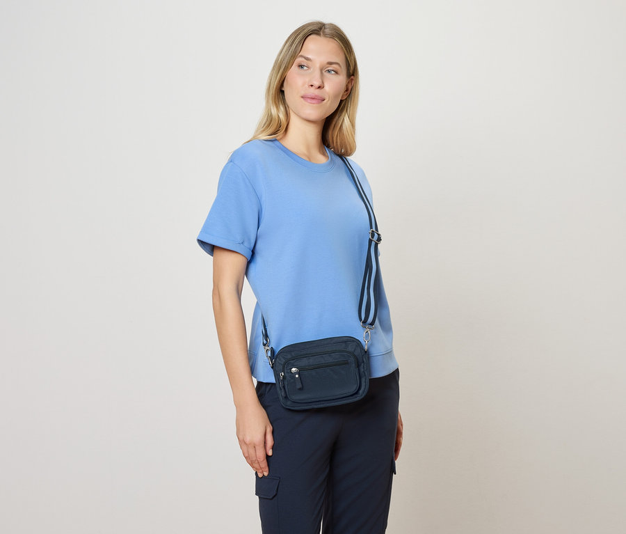 Frau mit hellblauer Bluse und marineblauer Umhängetasche mit blau-weißem Gurt.