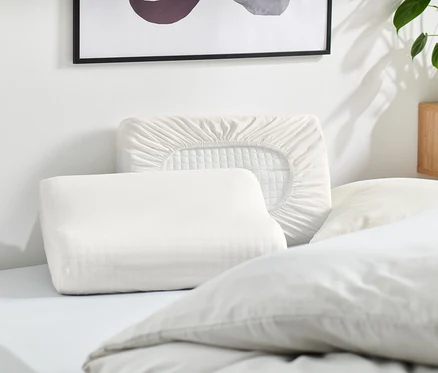 Mehrere weiße Kissen und ein weißer Kissenbezug liegen auf einem Bett.
