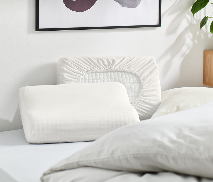 Mehrere weiße Kissen und ein weißer Kissenbezug liegen auf einem Bett.