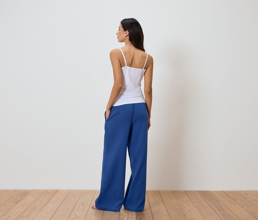 Frau von hinten in weißem Top und blauer Hose vor einer weißen Wand.