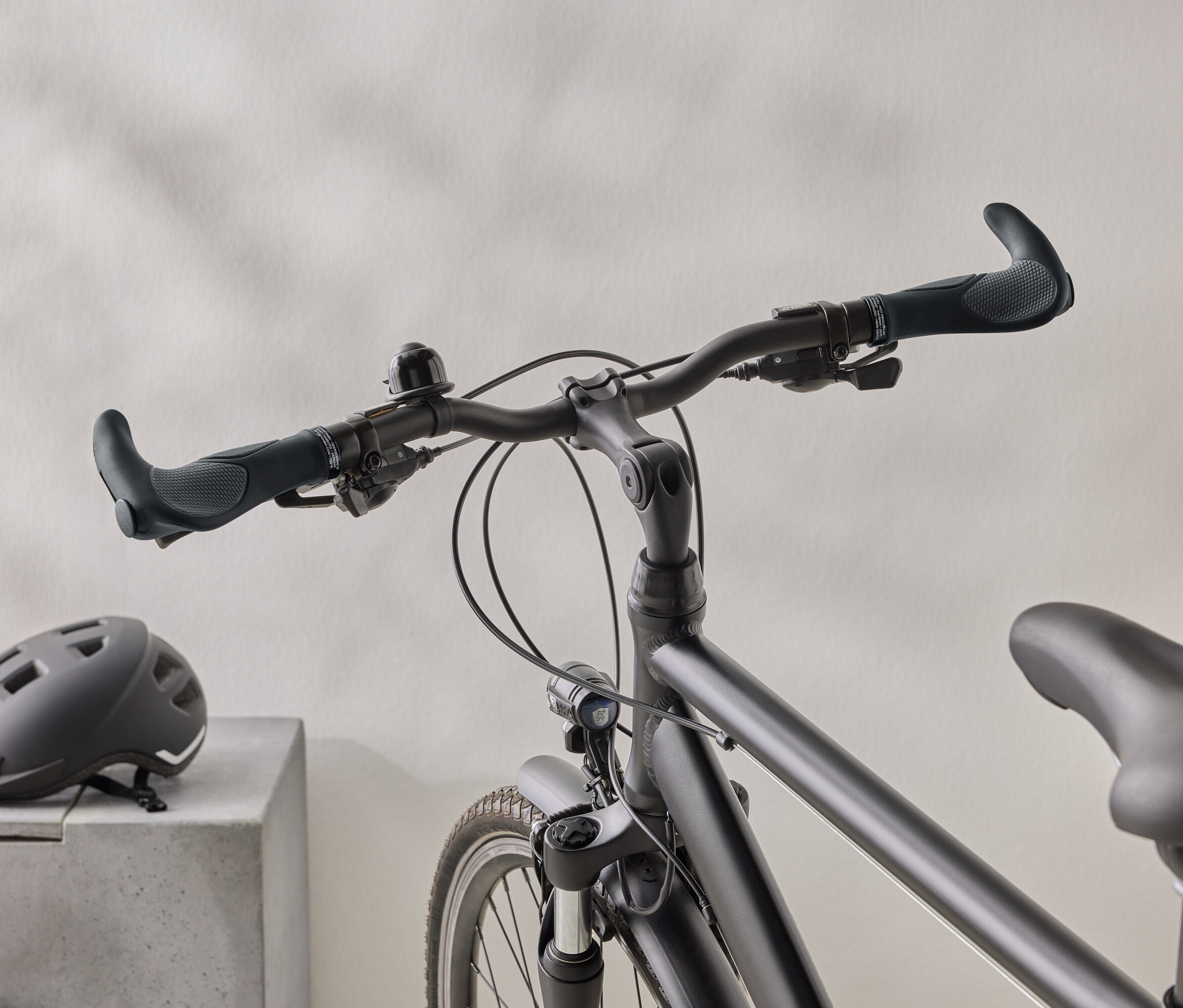 Nahaufnahme eines mattschwarzen Fahrrads mit einem schwarzen Helm auf einer Betonoberfläche im Hintergrund.