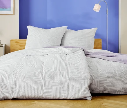 Ein Bett mit weißer Bettwäsche mit geometrischem Muster und zwei Kissen steht vor einer blauen Wand.