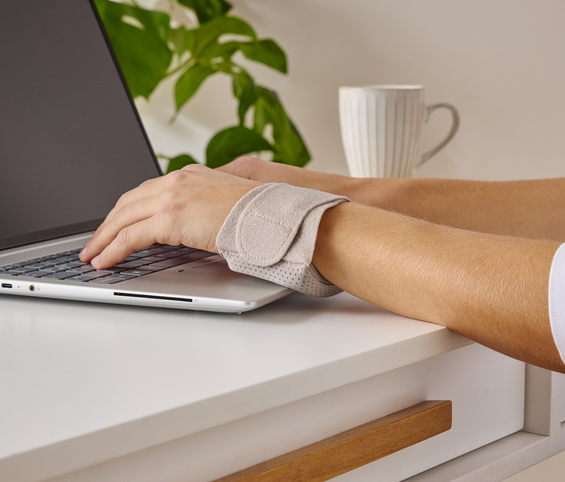 Person tippt auf einem Laptop und trägt eine Handgelenkstütze.