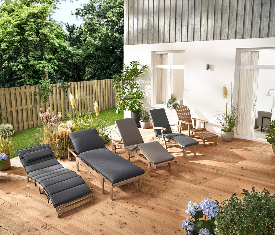 Mehrere Gartenliegen und ein Adirondack Gartensessel mit ausziehbarer Fußlehne aus Holz stehen auf einer Holzterrasse.