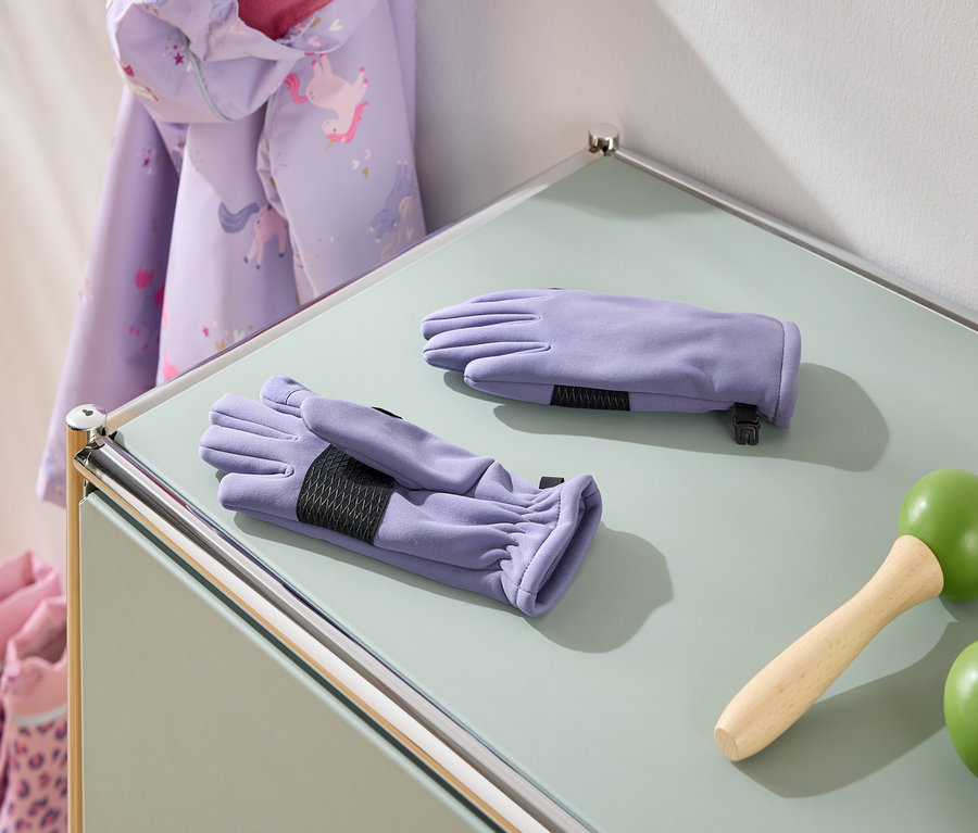 Auf einem Tisch liegen lila Handschuhe, ein Springseil mit grünen Griffen, eine Jacke mit Einhornmuster und rosa Stiefel.