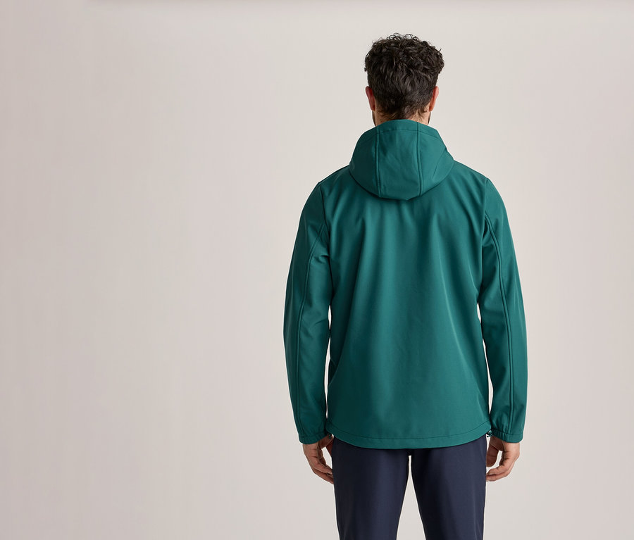 Ein Mann von hinten, der eine grüne Kapuzenjacke und dunkelblaue Hosen trägt.