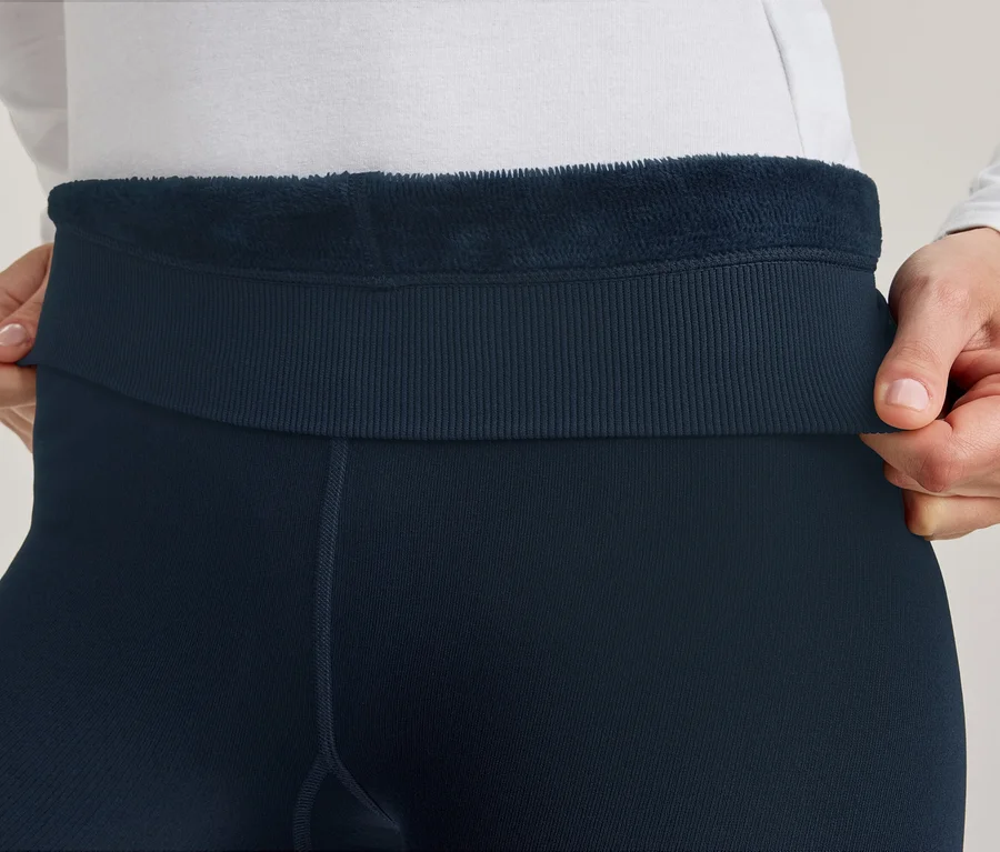 Hände ziehen am gerippten Bund einer dunkelblauen Leggings, um das flauschige marineblaue Fleecefutter innen zu zeigen.