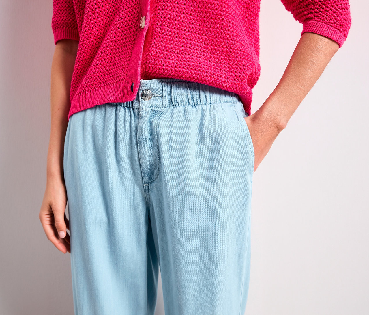 Eine Person trägt einen leuchtend pinken Strickcardigan und hellblaue Street One Jeans »Emee« mit Gummibund. Eine Hand steckt in der Hosentasche.