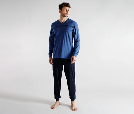 Ein Mann in einem blauen Langarm-V-Ausschnitt-Shirt mit horizontalem Streifendetail und dunkelblauer Jogginghose, barfuß stehend. Er blickt nach rechts.