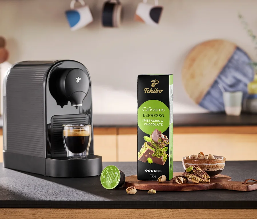 Kaffeemaschine gießt Kaffee in eine Tasse neben Packung Cafissimo Flavoured Espresso - Pistachio & Chocolate.