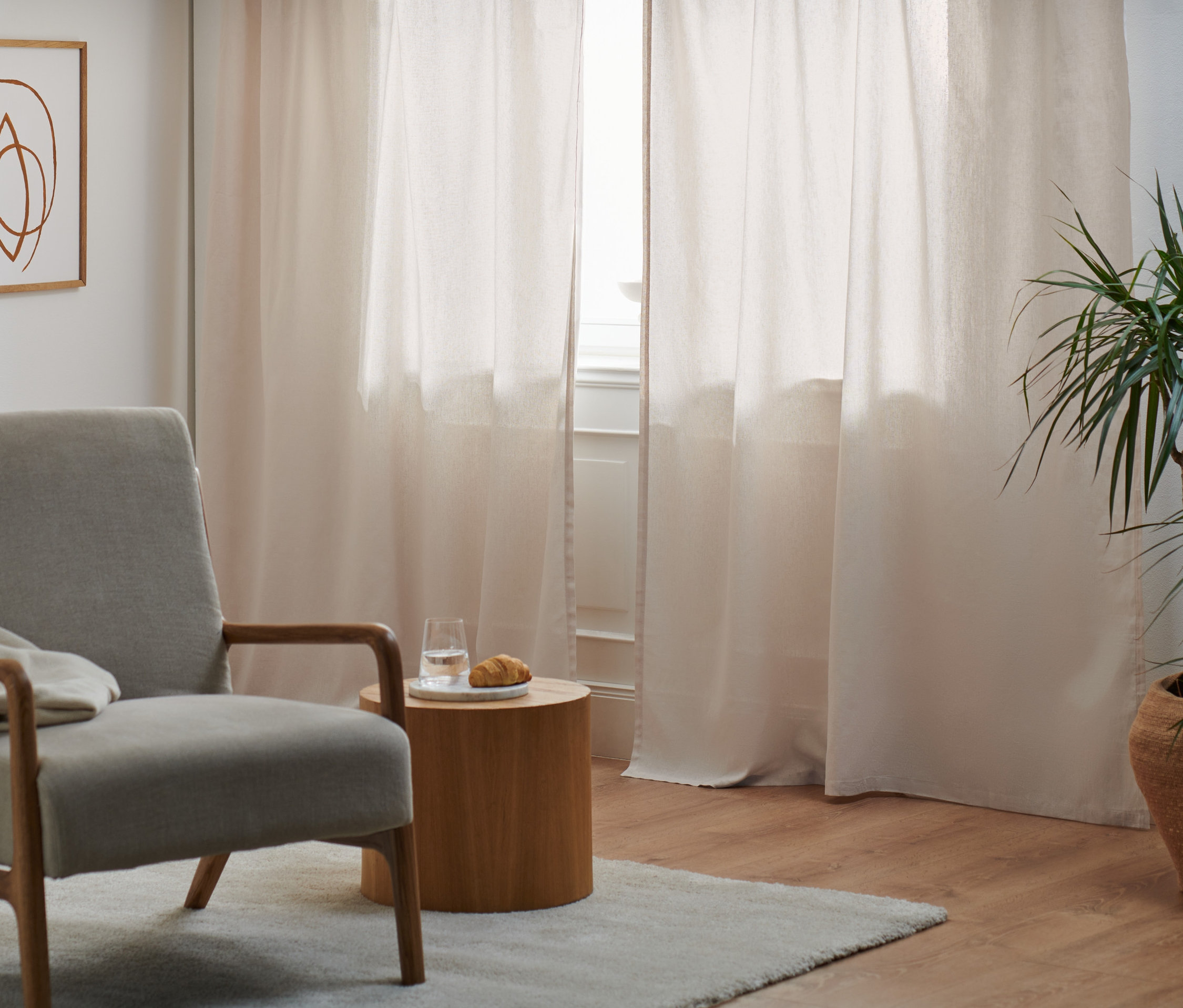 Grauer Sessel steht neben einem Fenster mit zwei Halbleinen-Vorhangschals.