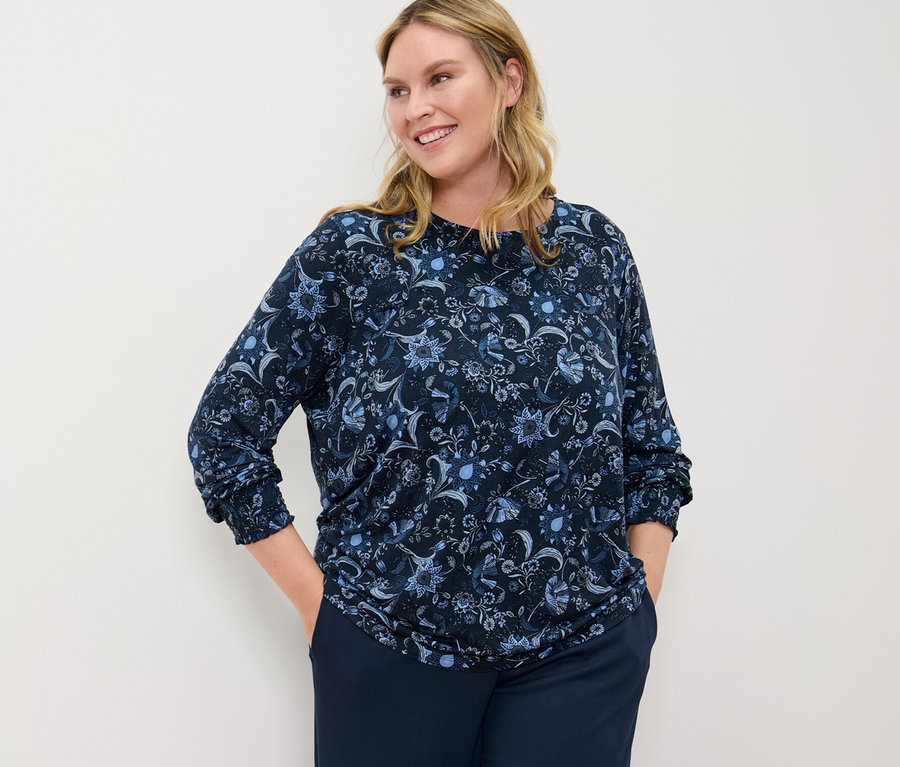 Frau posiert in einem bedruckten Blusenshirt und einer Komfort-Jerseyhose.