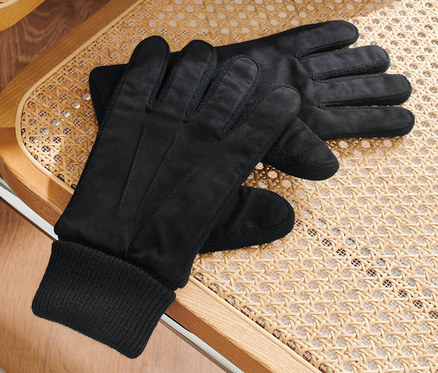 Schwarze Handschuhe liegen auf einem Rattanstuhl, über dem eine grüne Jacke hängt.