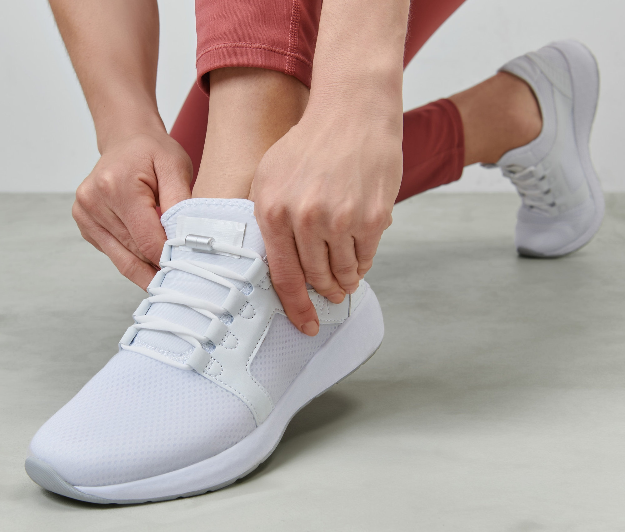 Frau schließt elastische Schnürsenkel an einem weißen Schuh.