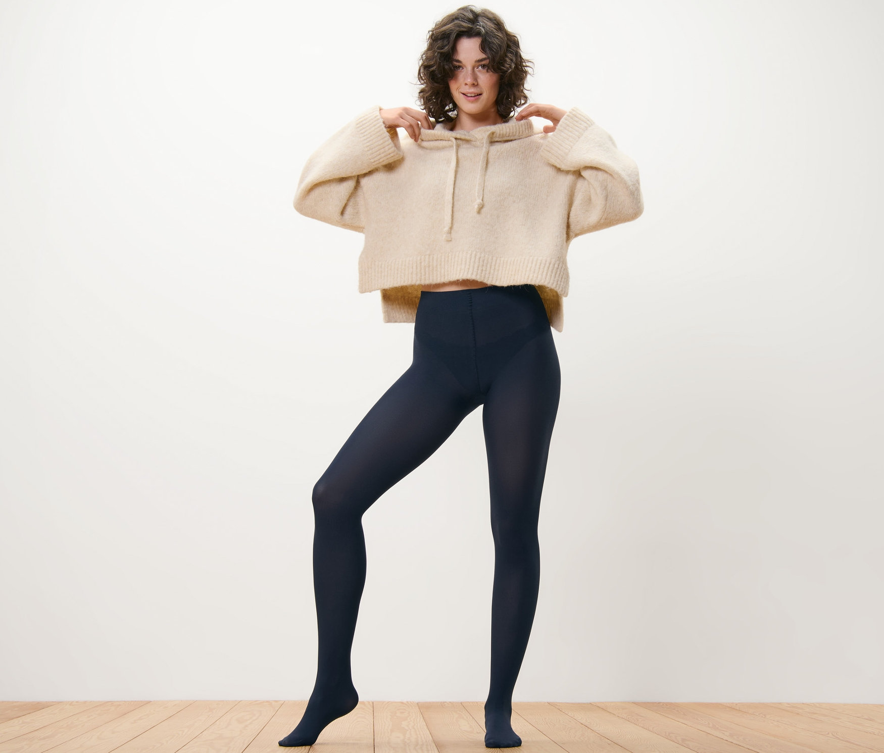 Frau posiert in beigem Hoodie und marineblauer Feinstrumpfhose, 80 DEN, 2 Paar.